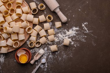Makarna ve yumurta, taze pişmiş. Buğdaydan ev yapımı makarna. Kahverengi arka planda el yapımı makarna bu fotoğrafın konusu. Erişteler çeşitli şekil ve boyutlarda.. 