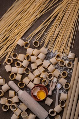 Makarna ve yumurta, taze pişmiş. Buğdaydan ev yapımı makarna. Kahverengi arka planda el yapımı makarna bu fotoğrafın konusu. Erişteler çeşitli şekil ve boyutlarda.. 