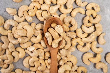 Gri mermer bir arka planda tahta kaşıkta kaju fıstığı. Bu görüntü sağlıklı bir çerez seçeneğini temsil ediyor ve beslenme, vejetaryenlik, doğal gıda ve sağlık gibi kavramları iletmek için kullanılabilir..