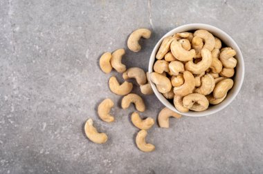Beyaz bir kasede kaju fıstığı, gri mermer bir arka planda tabak. Bu görüntü sağlıklı bir çerez seçeneğini temsil ediyor ve beslenme, vejetaryenlik, doğal gıda ve sağlık gibi kavramları iletmek için kullanılabilir..