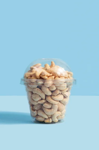 Kešu Ořechy Plastové Krabici Šálek Modrém Pozadí Tento Snímek Představuje — Stock fotografie