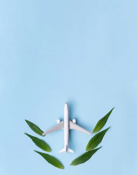 Stock image Sustainable Aviation Fuel. White airplane model, fresh green leaves on blue background. Clean and Green energy, Biofuel for aviation industry.