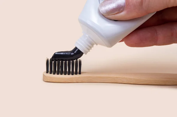 用黑色牙膏和竹子刷的白色管 背景是米黄色的黑色刚毛 简约主义牙科保健 — 图库照片