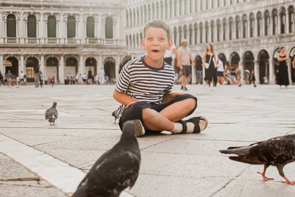 Venedik 'teki St. Mark Meydanı' nda oturmuş güvercinlerle oynayan çizgili tişörtlü yedi yaşında tatlı bir çocuk. Çocuklarla Avrupa 'da turizm ve eğlence