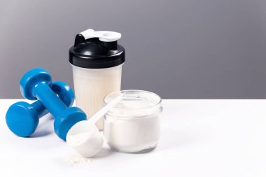 Spor besin: Proteinli içecek (kolajen). Bir spor mikseri, bir bardak ve spor için bir halter beyaz bir masada.