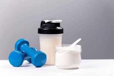 Spor besin: Proteinli içecek (kolajen). Bir spor mikseri, bir bardak ve spor için bir halter beyaz bir masada.