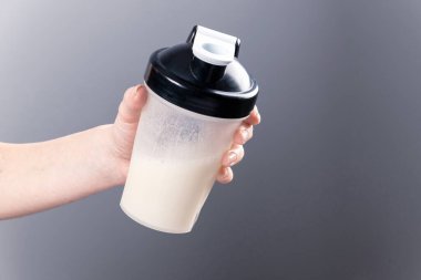 Bir kadın eli gri arka planda kolajenle karıştırıcı bardağı tutuyor. Spor besin: Proteinli içecek.