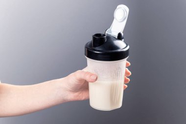 Bir kadın eli gri arka planda kolajenle karıştırıcı bardağı tutuyor. Spor besin: Proteinli içecek.