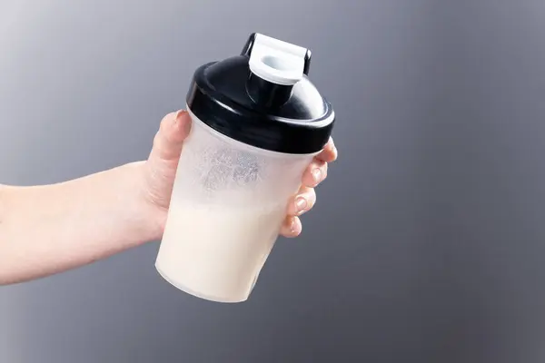 一只雌手拿着一只灰色背景上有胶原蛋白的混合玻璃杯 运动营养 含蛋白质的饮料 图库图片