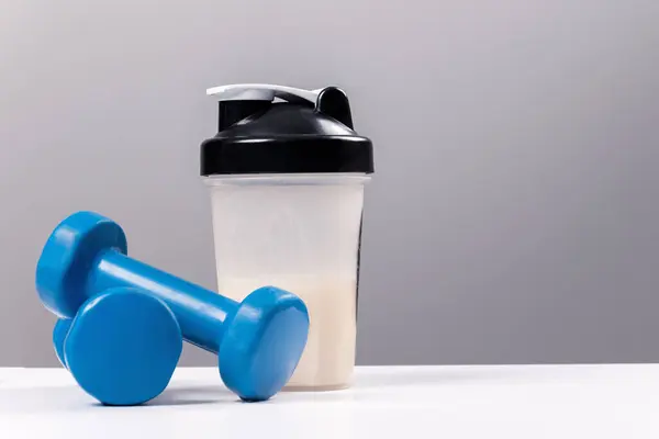 运动营养 含蛋白质 胶原蛋白 的饮料 一个运动混合器 一个杯子和一个健身哑铃放在了一张白色的桌子上 免版税图库照片