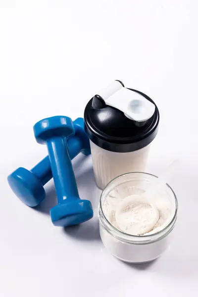 运动营养 含蛋白质 胶原蛋白 的饮料 一个运动混合器 一个杯子和一个健身哑铃放在了一张白色的桌子上 免版税图库照片