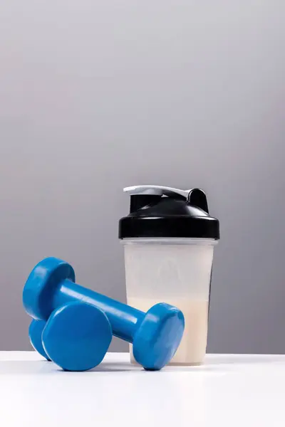 运动营养 含蛋白质 胶原蛋白 的饮料 一个运动混合器 一个杯子和一个健身哑铃放在了一张白色的桌子上 免版税图库图片