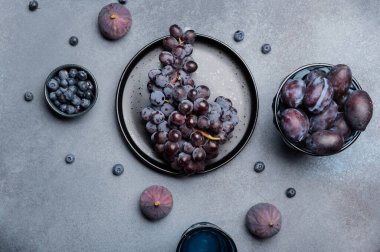 Taze koyu üzüm, incir, yaban mersini ve eriklerin kır taşından yapılmış arka plan manzarası. Mevsimlik meyveler, sonbahar yemek fotoğrafçılığı, sağlıklı beslenme kavramları ve organik ürün tanıtımı için mükemmel.