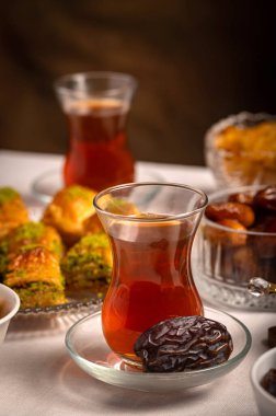 Bir bardak Türk siyah çayının yakınında, içi doğu tatlısı, kurutulmuş meyve ve fındık dolu hurma meyveleriyle servis edilir. Masa örtüsü üzerindeki zarif kompozisyon, Ramazan ayını resmetmek için mükemmel.