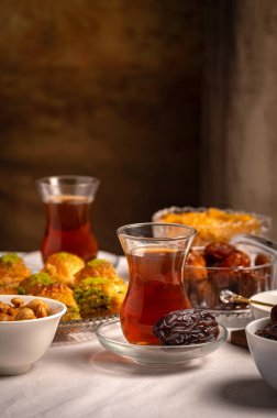 Bir bardak Türk siyah çayının yakınında, içi doğu tatlısı, kurutulmuş meyve ve fındık dolu hurma meyveleriyle servis edilir. Masa örtüsü üzerindeki zarif kompozisyon, Ramazan ayını resmetmek için mükemmel.