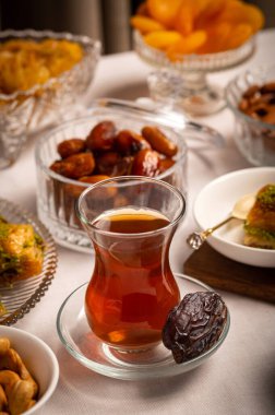 Bir bardak Türk siyah çayının yakınında, içi doğu tatlısı, kurutulmuş meyve ve fındık dolu hurma meyveleriyle servis edilir. Masa örtüsü üzerindeki zarif kompozisyon, Ramazan ayını resmetmek için mükemmel.