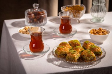 Bir bardak Türk siyah çayının yakınında, içi doğu tatlısı, kurutulmuş meyve ve fındık dolu hurma meyveleriyle servis edilir. Masa örtüsü üzerindeki zarif kompozisyon, Ramazan ayını resmetmek için mükemmel.