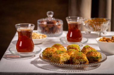 Bir bardak Türk siyah çayının yakınında, içi doğu tatlısı, kurutulmuş meyve ve fındık dolu hurma meyveleriyle servis edilir. Masa örtüsü üzerindeki zarif kompozisyon, Ramazan ayını resmetmek için mükemmel.