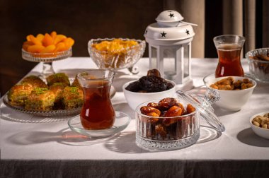 Bir bardak Türk siyah çayının yakınında, içi doğu tatlısı, kurutulmuş meyve ve fındık dolu hurma meyveleriyle servis edilir. Masa örtüsü üzerindeki zarif kompozisyon, Ramazan ayını resmetmek için mükemmel.