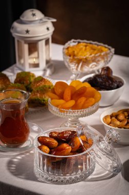 Bir bardak Türk siyah çayının yakınında, içi doğu tatlısı, kurutulmuş meyve ve fındık dolu hurma meyveleriyle servis edilir. Masa örtüsü üzerindeki zarif kompozisyon, Ramazan ayını resmetmek için mükemmel.
