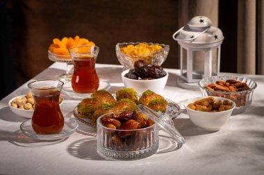 Bir bardak Türk siyah çayının yakınında, içi doğu tatlısı, kurutulmuş meyve ve fındık dolu hurma meyveleriyle servis edilir. Masa örtüsü üzerindeki zarif kompozisyon, Ramazan ayını resmetmek için mükemmel.