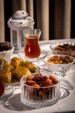 Bir bardak Türk siyah çayının yakınında, içi doğu tatlısı, kurutulmuş meyve ve fındık dolu hurma meyveleriyle servis edilir. Masa örtüsü üzerindeki zarif kompozisyon, Ramazan ayını resmetmek için mükemmel.