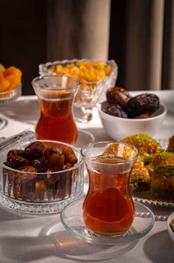 Bir bardak Türk siyah çayının yakınında, içi doğu tatlısı, kurutulmuş meyve ve fındık dolu hurma meyveleriyle servis edilir. Masa örtüsü üzerindeki zarif kompozisyon, Ramazan ayını resmetmek için mükemmel.