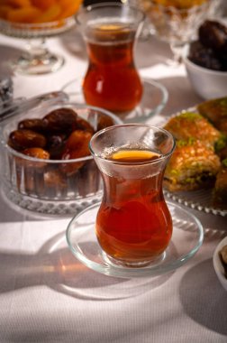 Bir bardak Türk siyah çayının yakınında, içi doğu tatlısı, kurutulmuş meyve ve fındık dolu hurma meyveleriyle servis edilir. Masa örtüsü üzerindeki zarif kompozisyon, Ramazan ayını resmetmek için mükemmel.