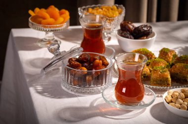 Bir bardak Türk siyah çayının yakınında, içi doğu tatlısı, kurutulmuş meyve ve fındık dolu hurma meyveleriyle servis edilir. Masa örtüsü üzerindeki zarif kompozisyon, Ramazan ayını resmetmek için mükemmel.