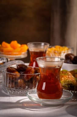 Bir bardak Türk siyah çayının yakınında, içi doğu tatlısı, kurutulmuş meyve ve fındık dolu hurma meyveleriyle servis edilir. Masa örtüsü üzerindeki zarif kompozisyon, Ramazan ayını resmetmek için mükemmel.