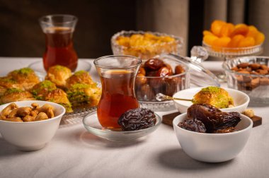 Bir bardak Türk siyah çayının yakınında, içi doğu tatlısı, kurutulmuş meyve ve fındık dolu hurma meyveleriyle servis edilir. Masa örtüsü üzerindeki zarif kompozisyon, Ramazan ayını resmetmek için mükemmel.