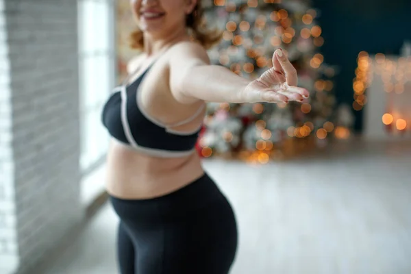 A beautiful fat woman in a sports uniform is exercising in the body to burn fat. Fitness and yoga. Sports at Christmas. High quality photo