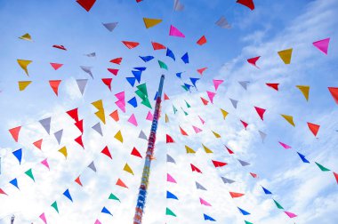 Tayland tarzı süslü parti bayrağının canlı rengi mavi gökyüzü ve beyaz bulutlu süslü bir direğin üzerindeki süslemeleri soyar.