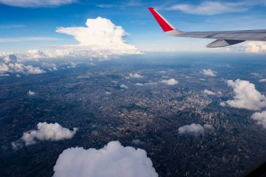 Kırmızı kanatlı mezun oldu. Koyu mavi gökyüzü. Aşağıdaki büyük şehrin güneş ışığı manzaralı.