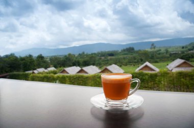 hot Thai's style milk tea in a cup with mountain view when a raining is coming from somewhere faraway