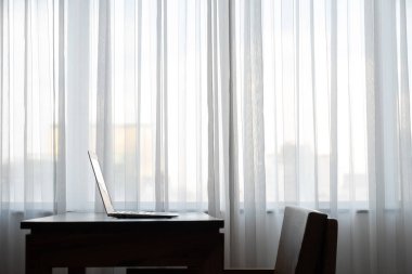 Büyük pencerenin yanındaki ahşap masanın üzerine koyulmuş bir defter. Büyük şehirdeki otel odasında ya da ofiste hiç kimse yoktu. 