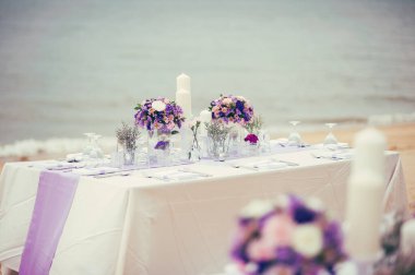 Romantik düğün resepsiyonunun yemek masası. Sahilde buketler, öğleden sonra da mavi deniz.