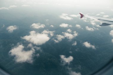 Uçağın manzarası bulutlarla kaplı bulutlu yeşil tepeleri gösteriyor.