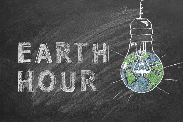 用粉笔画在学校黑板上的有字母Earth Hour手的灯泡 拯救世界 拯救我们的星球 免版税图库照片