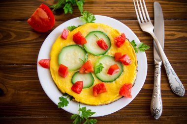 Fried omelet with zucchini, tomatoes, herbs in a plate on a wooden table.