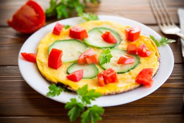 Fried omelet with zucchini, tomatoes, herbs in a plate on a wooden table.