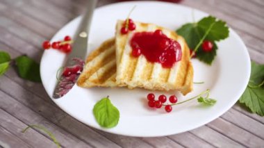 fried bread croutons for breakfast with redcurrant jam in a plate with berries on a wooden table.