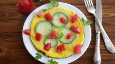 Fried omelet with zucchini, tomatoes, herbs in a plate on a wooden table.