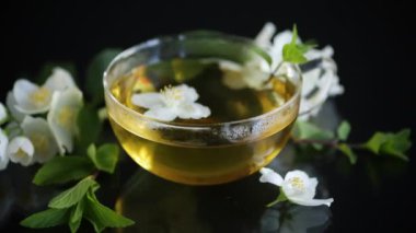 Siyah arka planda bir fincan yasemin çayı ve çiçekli kompozisyon