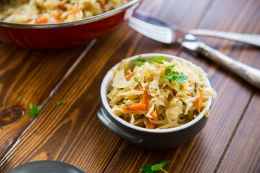 Tahta bir masada seramik bir kasede havuç, soğan ve otlarla haşlanmış lahana..