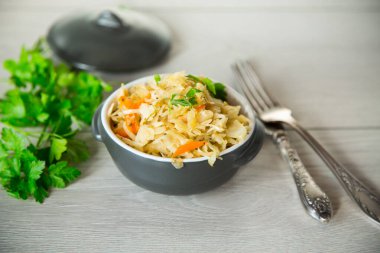 Tahta bir masada seramik bir kasede havuç, soğan ve otlarla haşlanmış lahana..