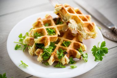 fried Belgian vegetable waffles with spices and herbs, in a plate on a light wooden table.