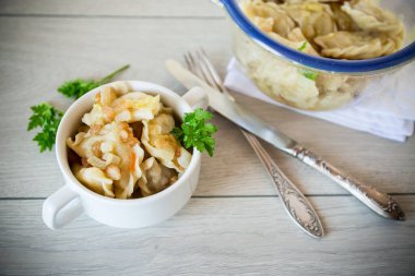 cooked dumplings with potatoes and fried onions, in a bowl on a wooden table.