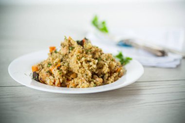 cooked bulgur with vegetables, carrots and dried mushrooms in a plate on a wooden table.