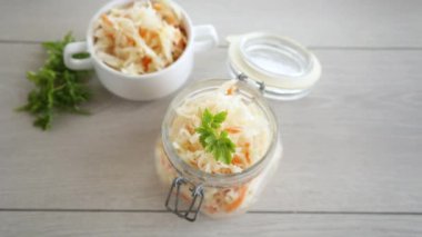 Sauerkraut with carrots and spices in a glass jar on a wooden table.